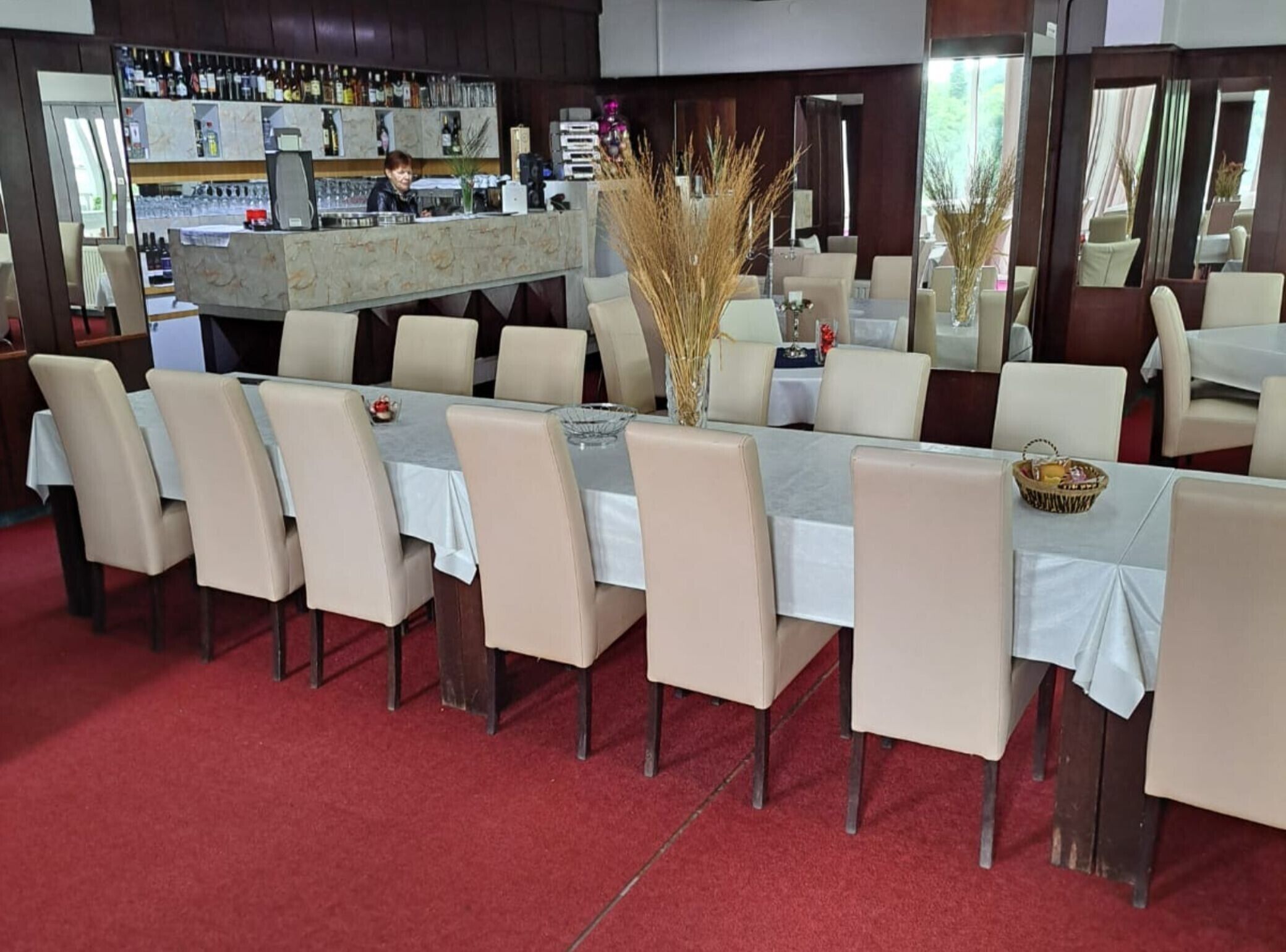 Un ristorante con area bar, diversi tavoli con sedie e un pavimento in moquette rossa.