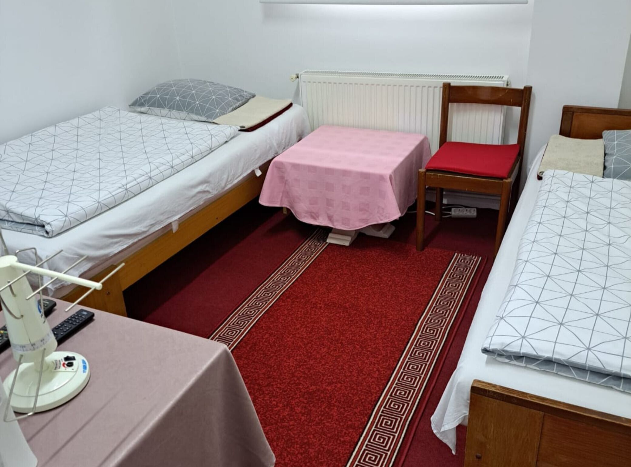 Et værelse med to senge, et lille bord med en lampe og en stol med en rød pude.