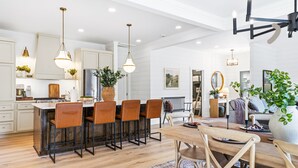 Een moderne keuken met een bar, een eethoek met een houten tafel en een zithoek met een bank en planten.
