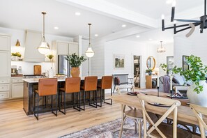 Une cuisine moderne avec un coin bar, un espace repas doté d’une table en bois, et un salon avec un canapé et des plantes.
