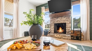 Een kamer met een open haard, een tafel met een kaasplank en een grote plant.