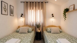 Ein Doppelzimmer mit zwei Betten, einem Nachttisch mit Lampe, einer Pflanze und einem 'Welcome'-Schild.