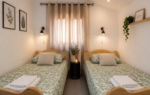 Ein Doppelzimmer mit zwei Betten, einem Nachttisch mit Lampe, einer Pflanze und einem 'Welcome'-Schild.