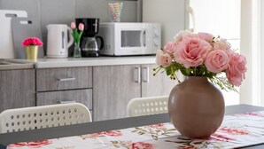 Eine Küche mit weißen Schränken, einer Mikrowelle, einer Kaffeemaschine und einem Tisch mit einer Vase mit rosa Blumen.