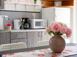 Eine Küche mit weißen Schränken, einer Mikrowelle, einer Kaffeemaschine und einem Tisch mit einer Vase mit rosa Blumen.