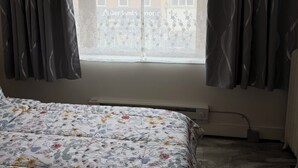 Een kamer met een bed, een raam met gordijnen en een radiator.