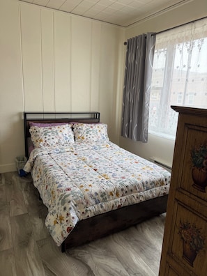 A bedroom with a wooden bed, a window with curtains, and a wooden dresser.