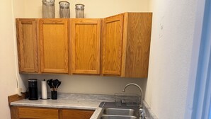 Een compacte keuken met houten kastjes, een spoelbak, een koffiezetapparaat en een prullenbak.