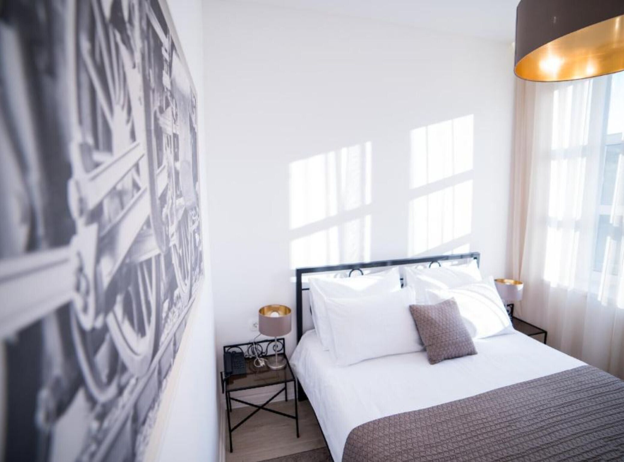 A hotel room with a bed, a nightstand, a lamp, and a large black-and-white artwork on the wall.
