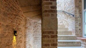Un escalier en pierre avec une rampe métallique et un luminaire fixé au mur.