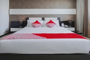 Ein ordentlich gemachtes Bett mit einer roten und weißen Tagesdecke, zwei passende Kissen und ein Nachttisch mit Lampe und Telefon.