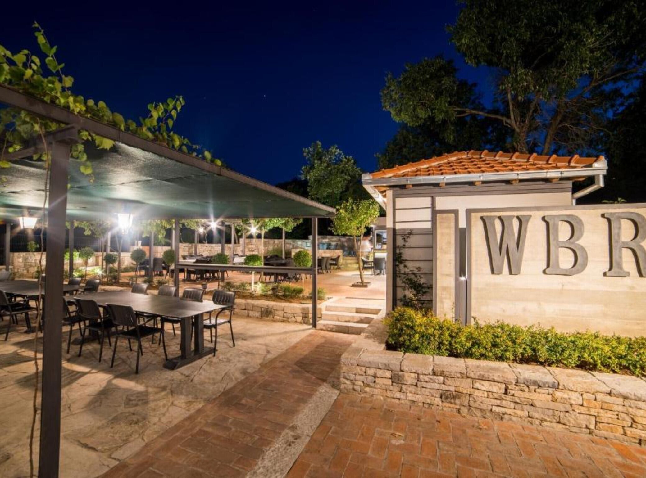 An outdoor dining area with tables and chairs, a covered seating area, and a building with a sign.