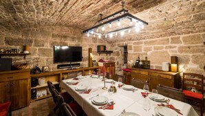 A stone-walled dining room with a long table set for a meal, a television, and wooden cabinets. - Stanica – The Imperial Route Heritage Experience-Deluxe Suite (Ravno)