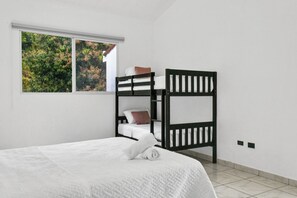 Una habitación con una cama individual, una litera, una ventana con vistas a árboles y suelo de baldosas.