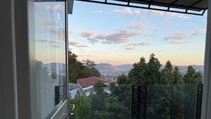 Ein Balkon mit Glasgeländer mit Blick auf eine Stadtlandschaft und Berge.