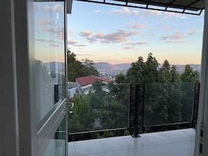 Ein Balkon mit Glasgeländer mit Blick auf eine Stadtlandschaft und Berge.