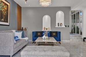 Una sala de estar moderna con un sofá gris, un sofá azul decorativo, una mesa de centro y una araña.