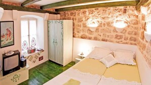 Un dormitorio con pared de piedra, cama con ropa de cama blanca, armario y una mesita de noche con lámpara.