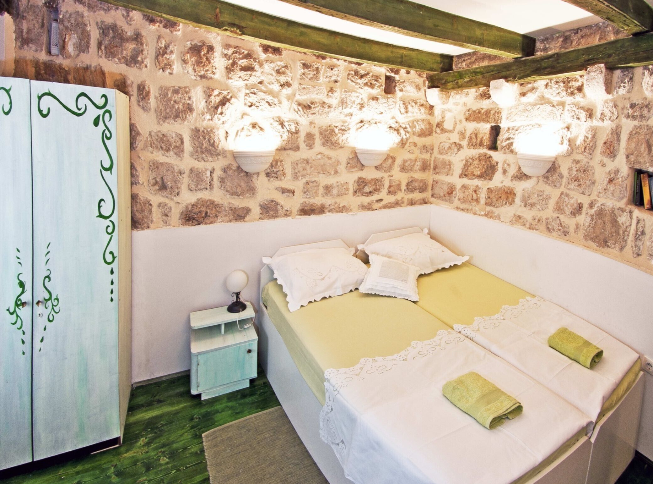 A bedroom with a stone wall, a bed with white linens, a small bedside table, and a wardrobe.