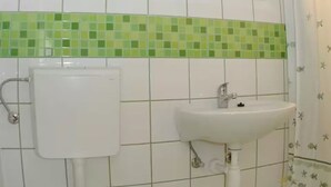 Un baño con lavamanos blanco, inodoro y salpicadero de azulejos verdes.
