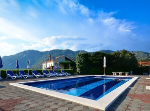 Une piscine entourée de montagnes et d’un bâtiment, avec des chaises longues et des parasols.