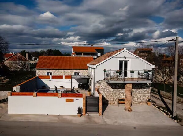 Une maison à deux étages avec une façade en pierre, un toit recouvert de tuiles rouges et un balcon.