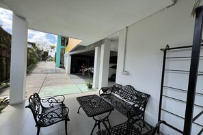 Un espace extérieur aménagé en terrasse, avec des meubles en métal, une vue sur la rue et l’entrée d’un immeuble.