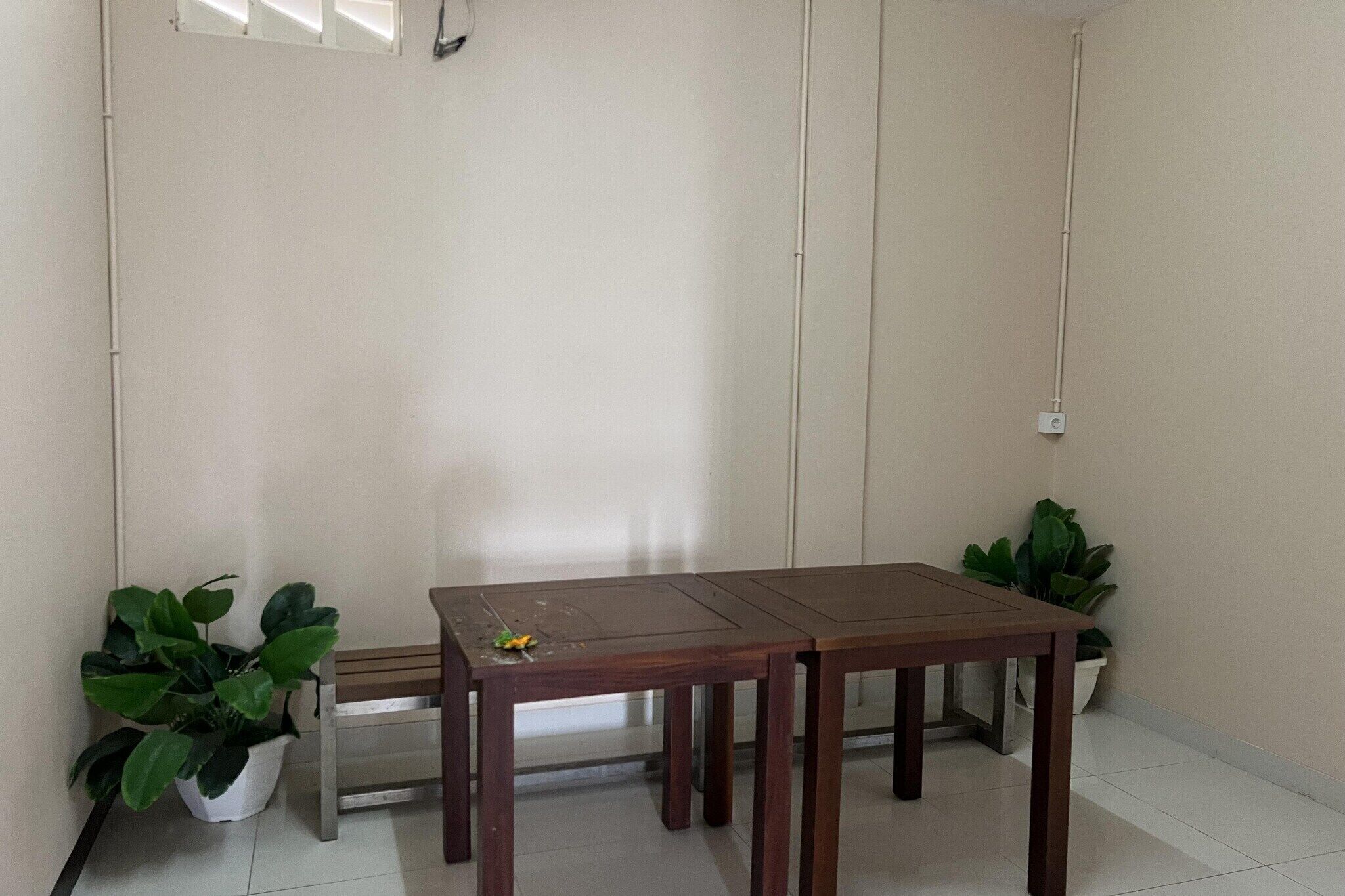 Une pièce avec une table en bois, deux plantes en pot, un banc et un luminaire fixé au mur.