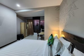 Une chambre d’hôtel avec un lit, une table de chevet, une lampe, une chaise et une vue sur l’extérieur.