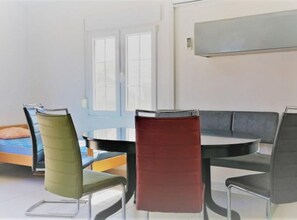 Ein stilvoller Essbereich mit einem runden Tisch und vier Stühlen, ein Bett mit blauer Bettwäsche und ein Fenster mit Jalousien.