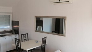 Un alojamiento pequeño, con una habitación individual, una kitchenette, una mesa de comedor con cuatro sillas, una cama individual con almohada y un espejo en la pared.