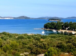 A coastal landscape with a clear view of the sea, a small island with trees, and a few boats. - Guest House Jurković - One Bedroom Apartment with Terrace (Pirovac)