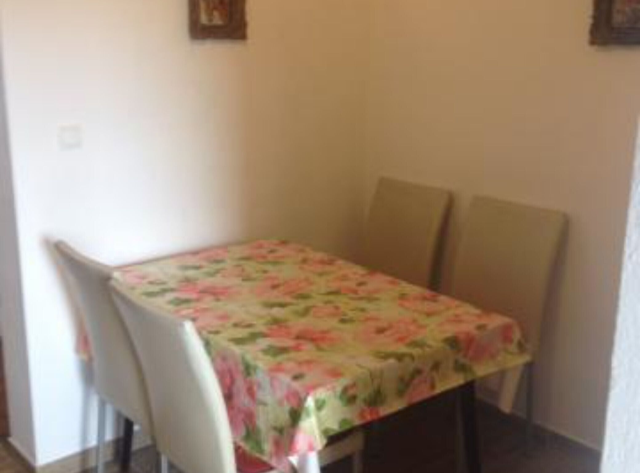 A dining area with a table covered by a floral tablecloth, two chairs, and a wall-mounted picture.