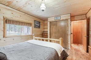 A wooden cabin bedroom with a bed, a window with a view, a door, and a sign that says 'Blessed'. - Rugers Retreat | Fire Pit | Grill | 35 Mins To YNP (Island Park)