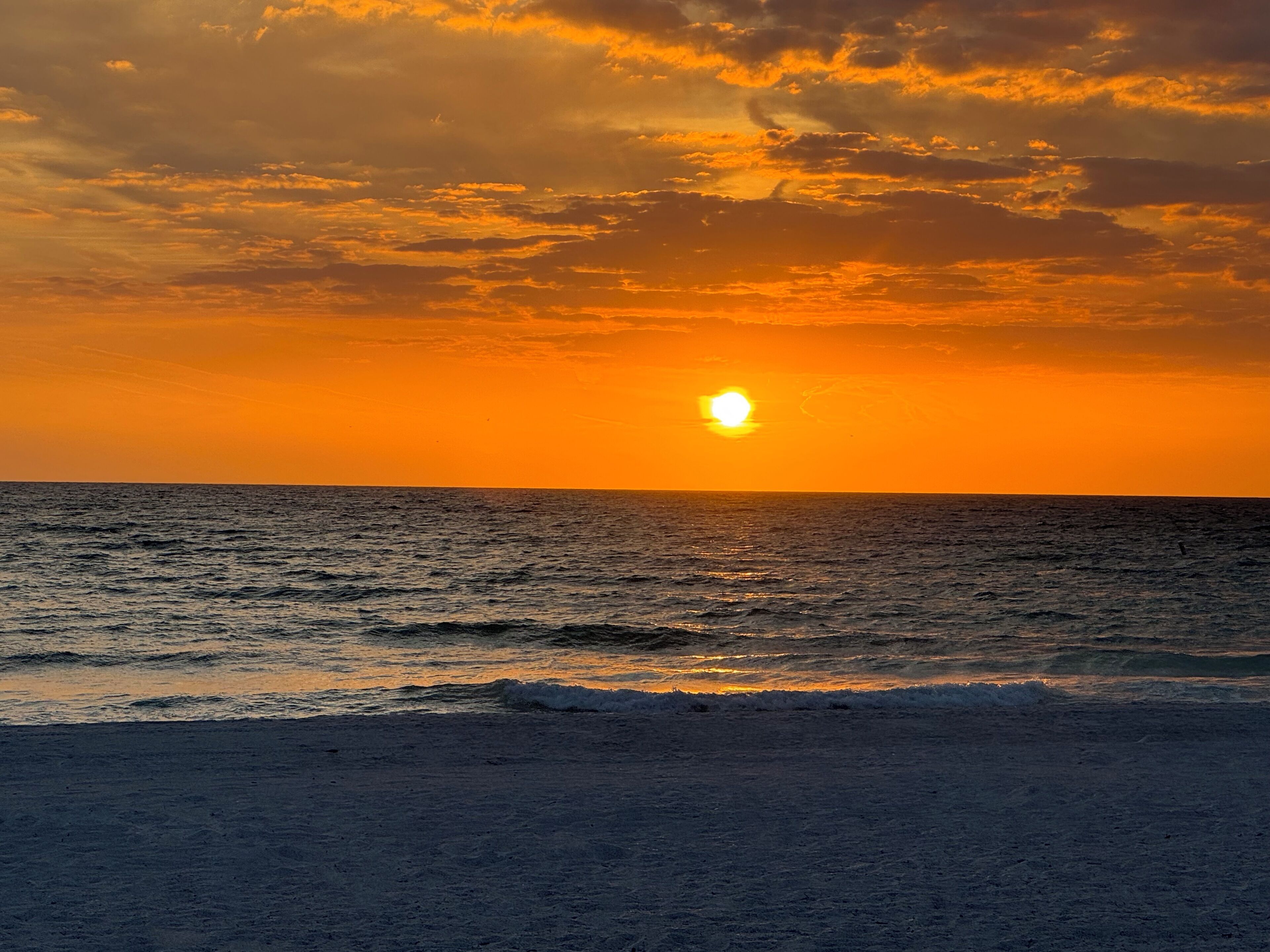 Een zonsondergang boven de oceaan, met golven die de kust naderen.