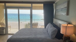 Et hotelværelse med en seng, en lampe, et billede og udsigt til stranden og havet.