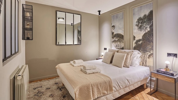 Ein Schlafzimmer mit einem großen Bett, einem Nachttisch mit Lampe, einem Spiegel und Kunstwerken an der Wand.
