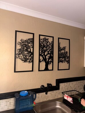 A kitchen with a sink, a dish rack, and three wall-mounted tree silhouettes. - Stylish Private Retreat Sleeps 3 Secure Work-Friendly Unique Design Stay (Johannesburg)