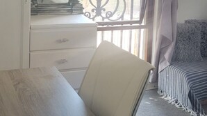 A room with a wooden table, a white chair, a mirror with a decorative frame, a window with a curtain, and a balcony railing. - Stylish Private Retreat Sleeps 3 Secure Work-Friendly Unique Design Stay (Johannesburg)