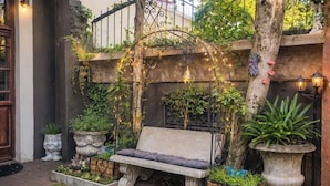 A garden with a bench, stone planters, and a wrought iron archway. - Stylish Private Retreat Sleeps 3 Secure Work-Friendly Unique Design Stay (Johannesburg)