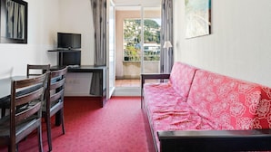 A room with a red patterned sofa, a TV on a stand, a dining table with chairs, and a view through an open door. - Chic Light-Filled Pool Oasis in Grasse (Grasse)