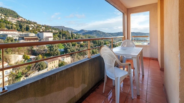 A balcony with a table and chairs, a view of a town and hills, and a clear sky. - Chic Light-Filled Pool Oasis in Grasse (Grasse)