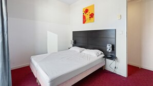 A single bed with a dark headboard, white bedding, a bedside table with a lamp, and a red carpeted floor. - Chic Light-Filled Pool Oasis in Grasse (Grasse)