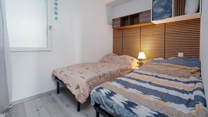 Een slaapkamer met een bed, nachtkastje, lamp, raam en een wandplank met kussens.