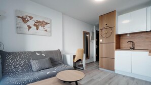Een moderne woonkamer met een bank, een ronde salontafel, een stoel en een keuken met witte kasten en een houten scheiding.