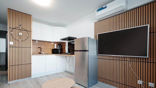 Een moderne keuken met een geïntegreerde koelkast, een koffiezetapparaat en een flatscreen televisie aan de wand.