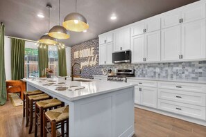 Una cucina moderna con mobili bianchi, un'isola centrale con sgabelli, illuminazione a sospensione e una parete di fondo con motivo geometrico.