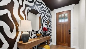 Ein Korridor mit Wand in Zebra-Muster, einer Holztür, einem Konsolentisch mit Lampe und einer kleinen Bank.