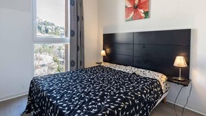 Een slaapkamer met een bed, twee bedlampen, een raam met uitzicht en een bloemschilderij aan de muur.