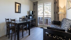 Een kamer met een eettafel, stoelen, een bank, een televisie en een balkon met uitzicht.